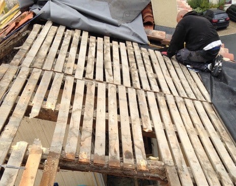 Rénovation de Toiture : Réparation de Charpente en Bois Un couvreur travaille sur une toiture en rénovation avec des lattes de bois apparentes et endommagées.