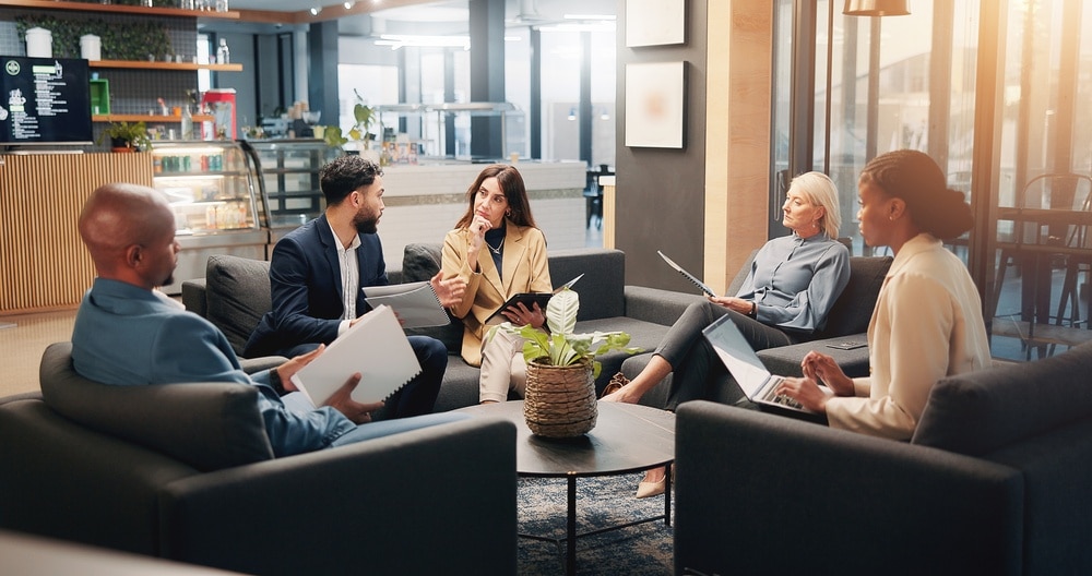 Réunion d'équipe collaborative dans un bureau moderne Cinq professionnels discutent autour d'une table dans un salon de bureau moderne avec des documents et un ordinateur.