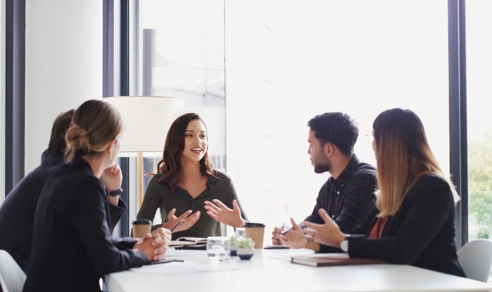Collaboration professionnelle en réunion d'affaires moderne Équipe diverse en réunion dans un bureau moderne, une femme s'exprimant avec enthousiasme lors d'un échange.
