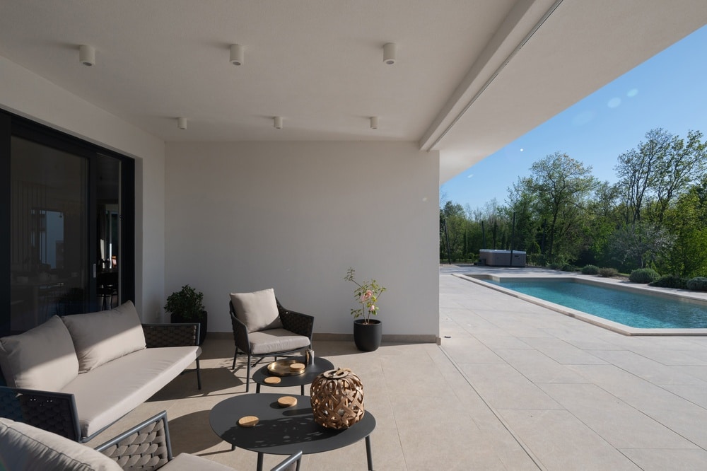 Terrasse Moderne avec Piscine et Salon de Jardin de Luxe Terrasse moderne avec salon de jardin gris, vue sur piscine rectangulaire et jardin verdoyant sous un ciel bleu.