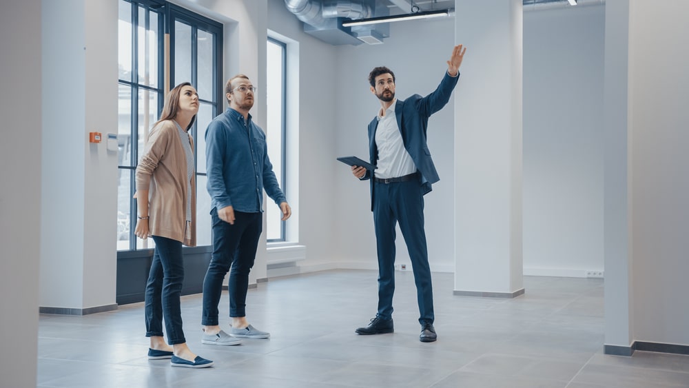 Visite d'un bureau moderne avec un agent immobilier Agent immobilier montrant un bureau moderne à un couple intéressé, geste indicatif avec tablette.